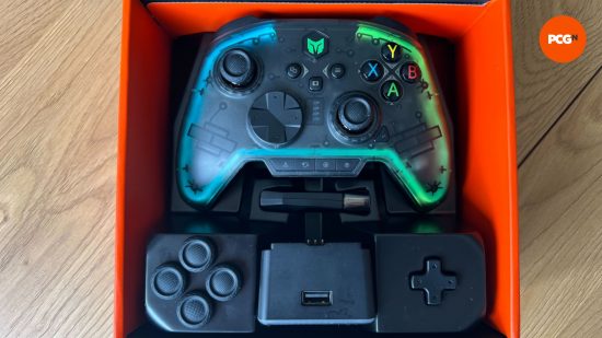 La manette Rainbow Pro 2 dans sa boîte avec des manettes supplémentaires, un D-pad et la station de chargement 