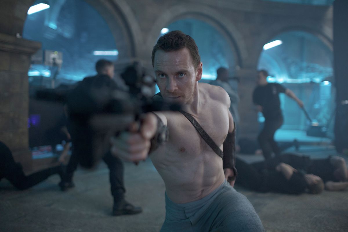 Cal Lynch (Michael Fassbender, torse nu et cheveux courts) se tient dans une pièce pleine d'arches de pierre, où des hommes en noir se battent ou ont été abattus en arrière-plan, et pointe un énorme pistolet flou vers la caméra dans Assassin's Creed, le film de 2016