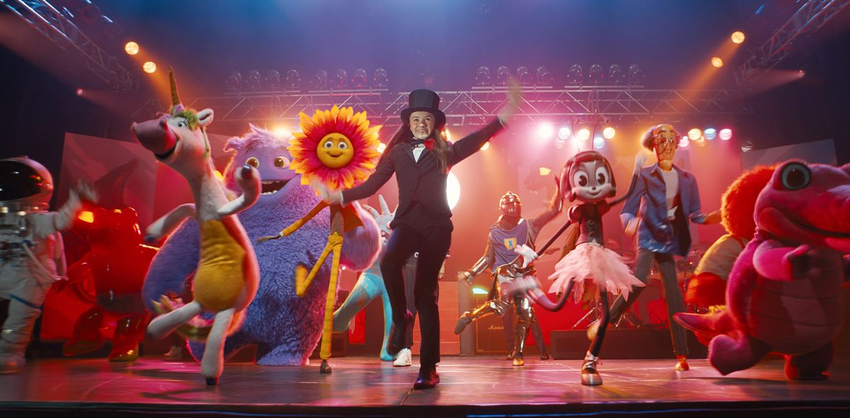 Bea (Cailey Fleming), en costume et haut-de-forme, danse sur scène sous des lumières vives, entourée de créations CG représentant les amis imaginaires des enfants : une licorne bipède à gros nez dans un body jaune, un astronaute, un tournesol avec un visage et des pattes, une grosse créature à fourrure violette, et plus encore