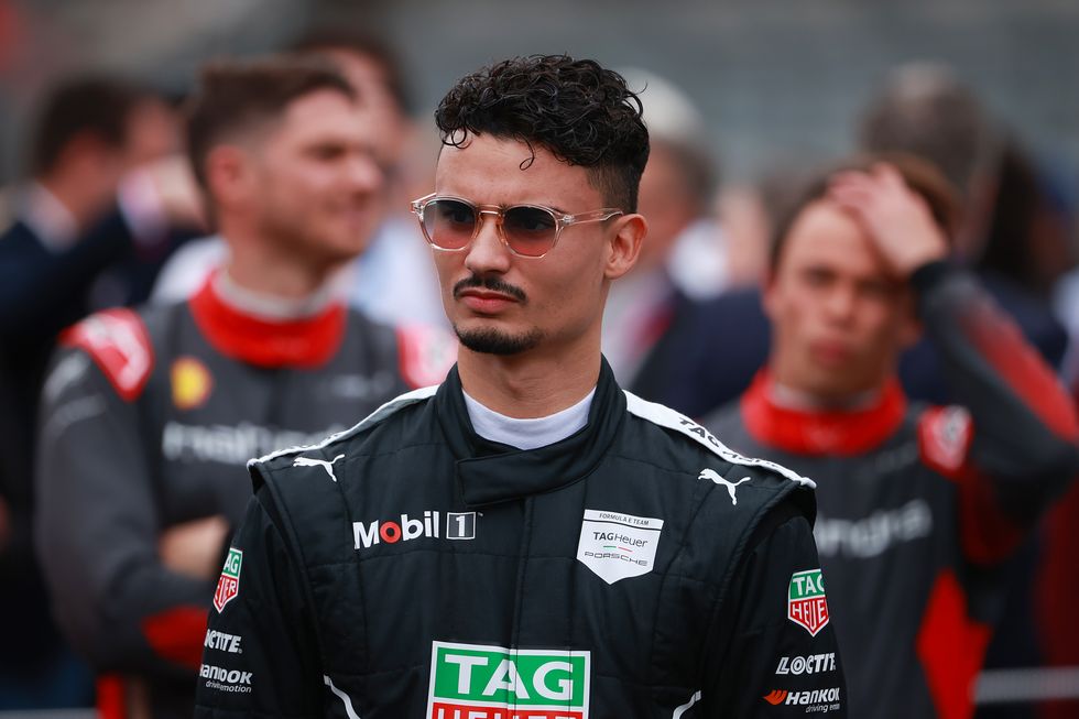 le pilote de formule e pascal wehrlein, portant sa combinaison de course et ses lunettes de soleil, a l'air pensif alors qu'il attend sur la grille devant un eprix