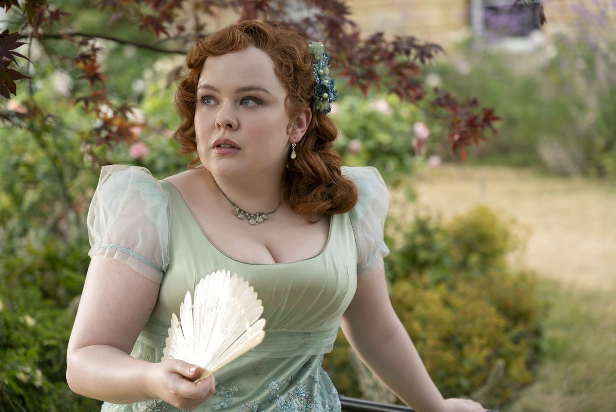 Nicola Coughlan dans le rôle de Penelope Featherington dans la saison 3 de Bridgerton. Elle porte une robe vert clair dans un jardin et s'éventre. 