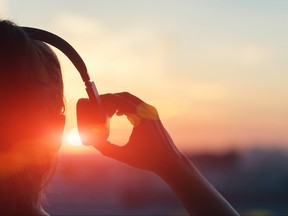 Femme soulevant un côté des écouteurs de l'oreille au coucher du soleil.