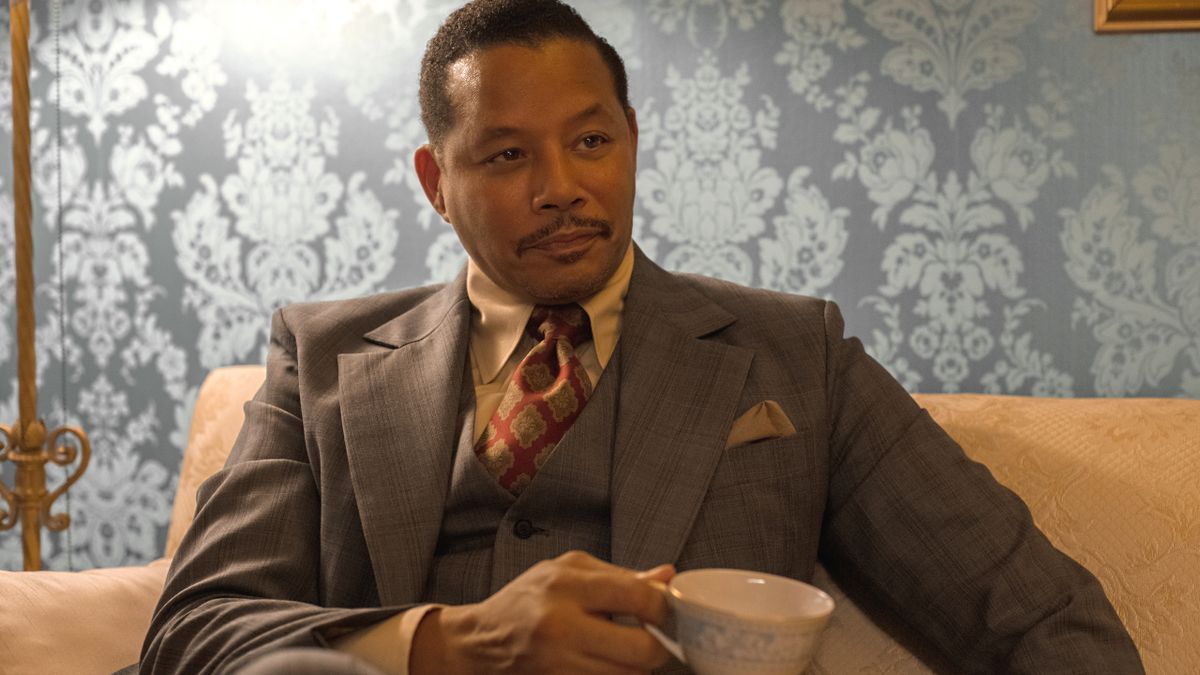 Terrence Howard sits on a couch, dressed in a suit and having a cup of coffee in Shirley.