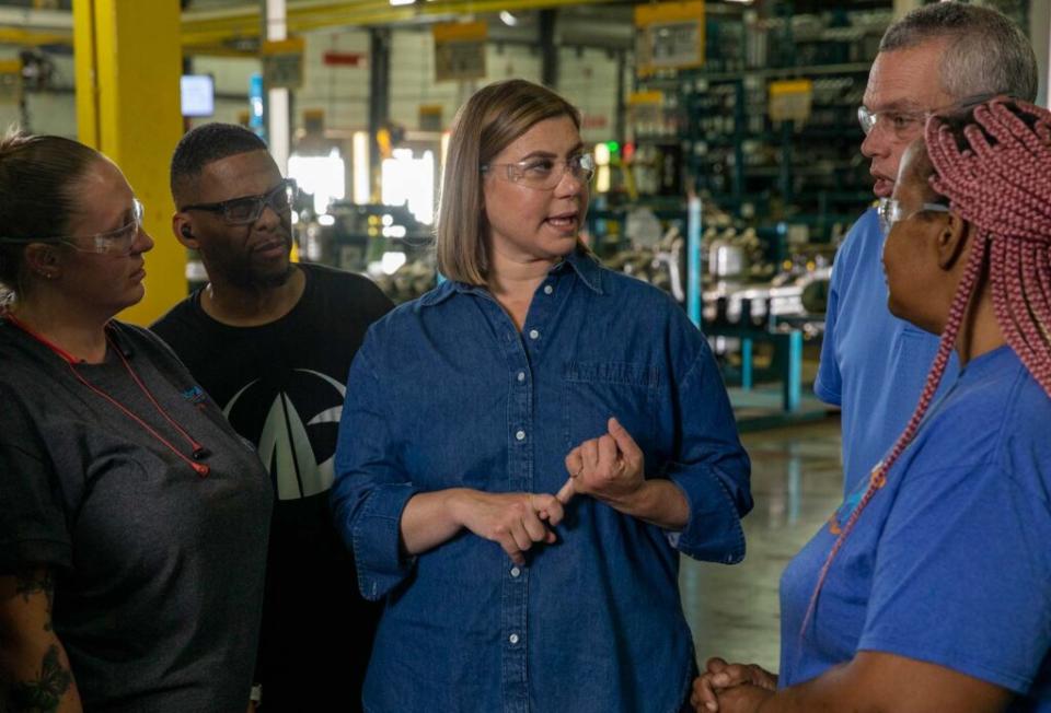 Photo de campagne pour la représentante américaine Elissa Slotkin.  Elle se tient dans une usine, porte des lunettes, discute avec plusieurs ouvriers.