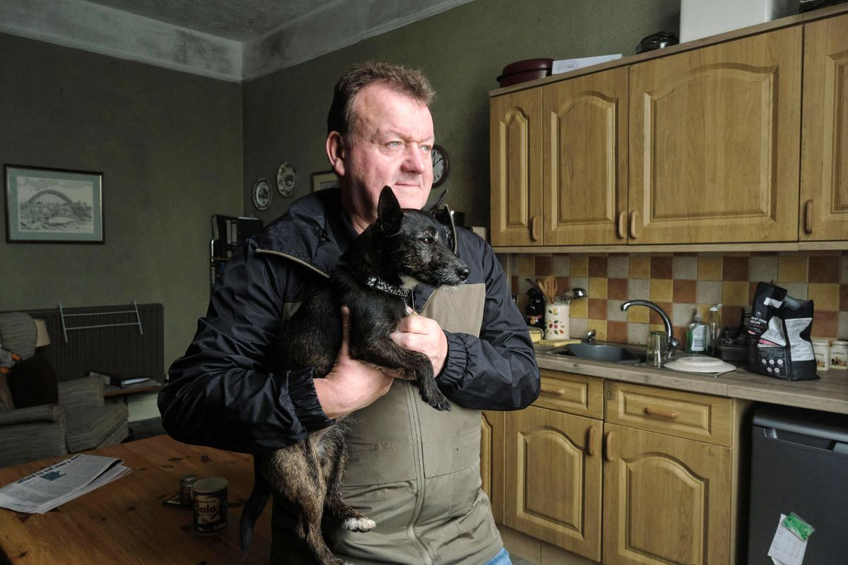 Un homme tenant un petit chien noir debout dans une cuisine