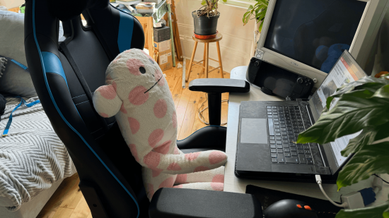 Une peluche était assise sur une chaise de jeu devant un bureau avec un ordinateur portable, un moniteur CRT et des plantes