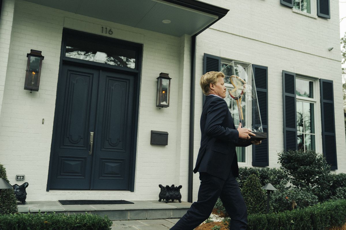 Jesse Plemons porte une raquette de tennis en bois cassée dans une vitrine devant une maison chic dans Kinds of Kindness