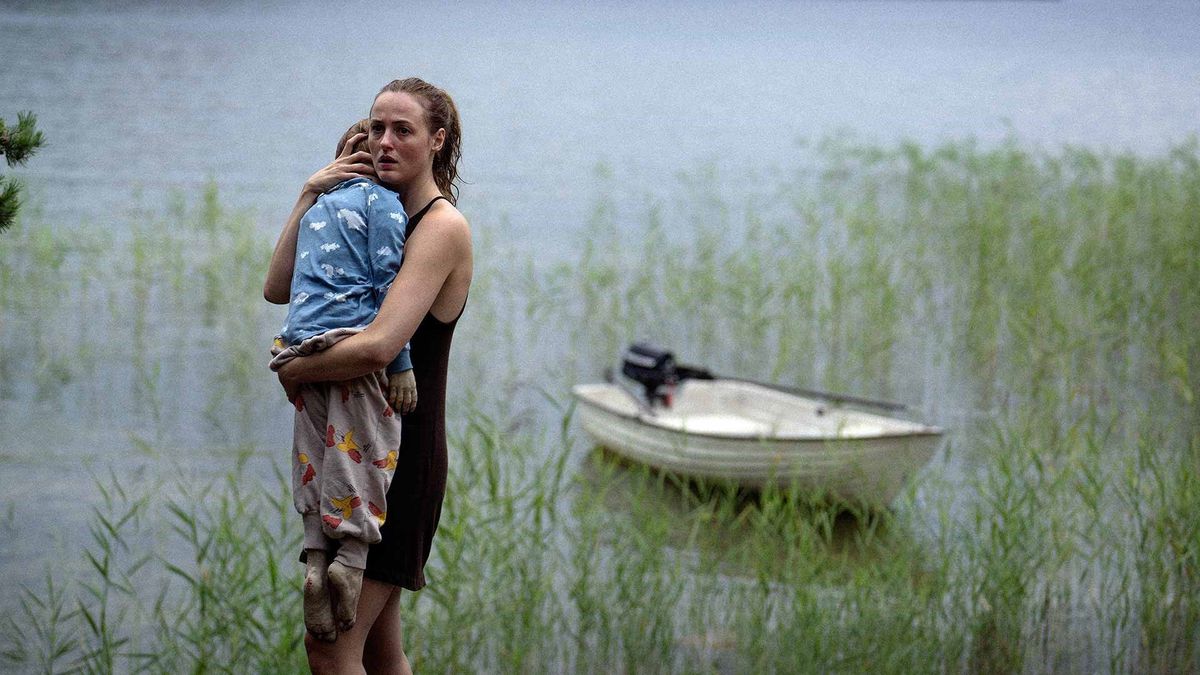 Une femme tenant le corps mou d'un enfant dans ses bras à côté d'un bateau entouré d'un marais de roseaux dans Handling the Undead.