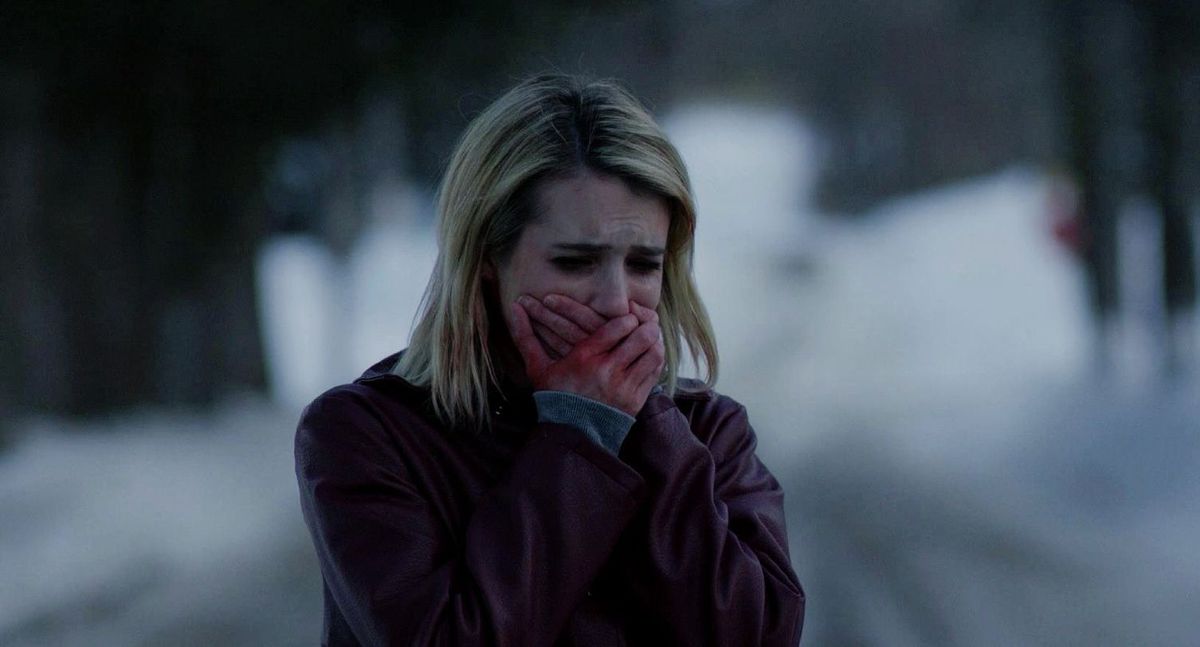 Une femme joignant ses mains tachées de rouge sur sa bouche avec un air de terreur visible tout en regardant quelque chose hors écran dans The Blackcoat's Daughter.