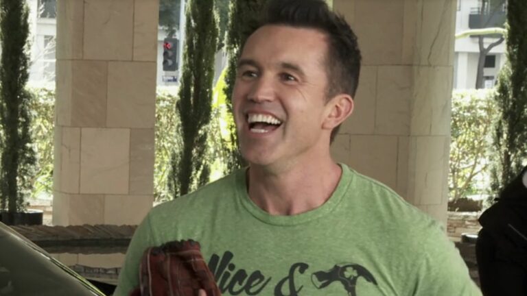 Mac smiling very wide as he holds a baseball glove while talking to Chase Utley outside a hotel in It