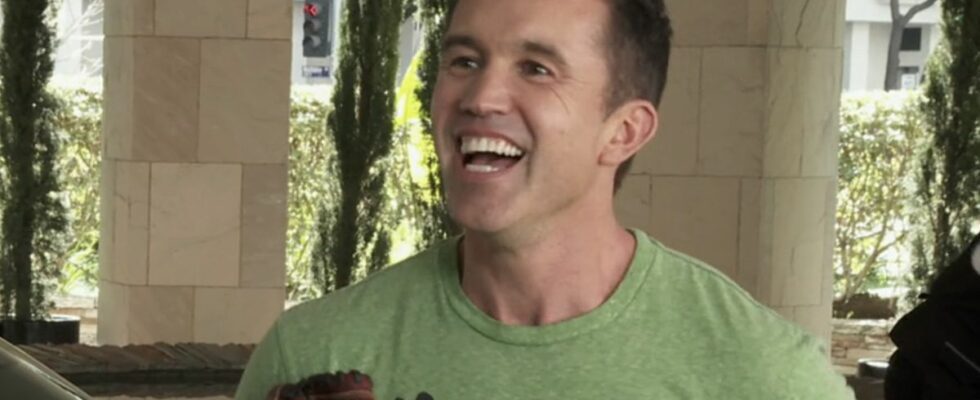 Mac smiling very wide as he holds a baseball glove while talking to Chase Utley outside a hotel in It