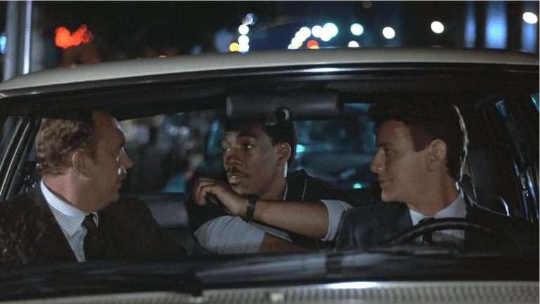 Eddie Murphy, Judge Reinhold, and John Ashton in a car talking in Beverly Hills Cop