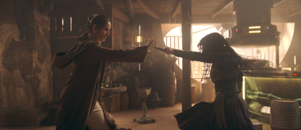 (De gauche à droite) : Le Maître Jedi Indara (Carrie-Anne Moss) et Mae (Amandla Stenberg) s'affrontent dans The Acolyte.  Indara tient le poignard tendu de Mae en utilisant la Force.