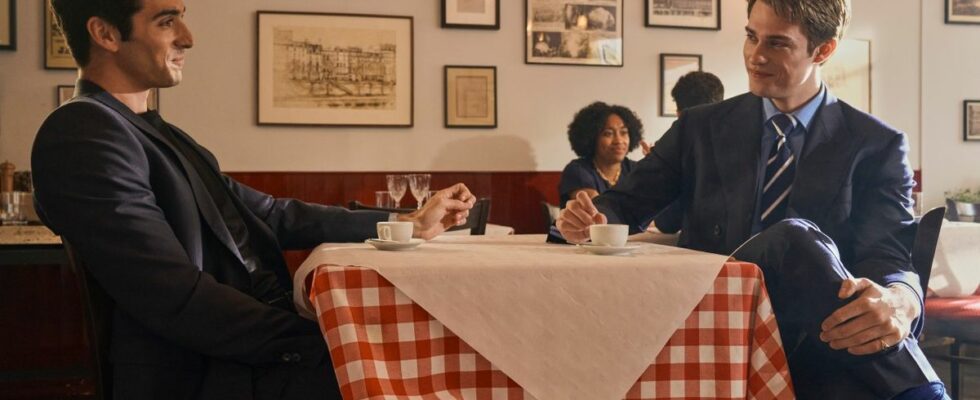 From left to right: Alex and Henry looking across a table at each other affectionately.