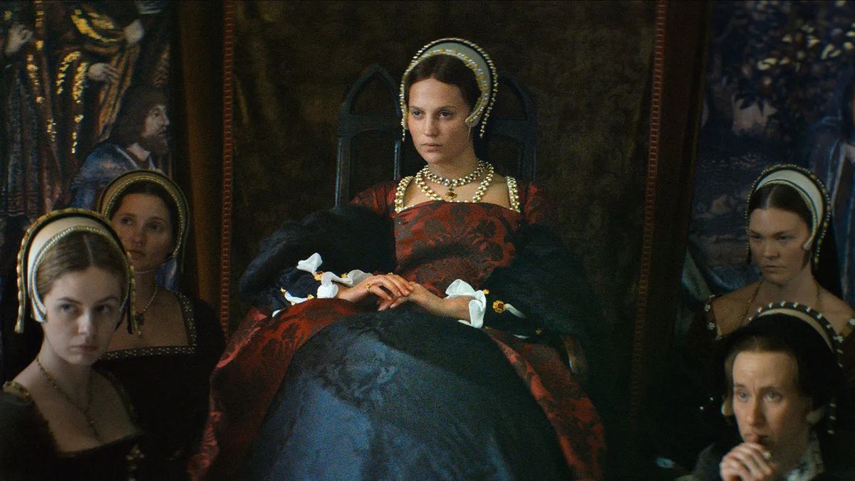 Une femme (Alicia Vikander) assise sur un petit trône flanquée de plusieurs autres femmes dans Firebrand.