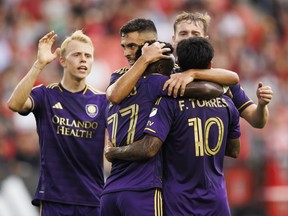 Le milieu de terrain de l'Orlando City SC, Martin Ojeda (deuxième à gauche), embrasse l'attaquant Ivan Angulo (77) et l'attaquant Facundo Torres (10) après avoir marqué le premier but contre le Toronto FC lors de la première mi-temps de leur match de football MLS à Toronto, mercredi 3 juillet 2024.