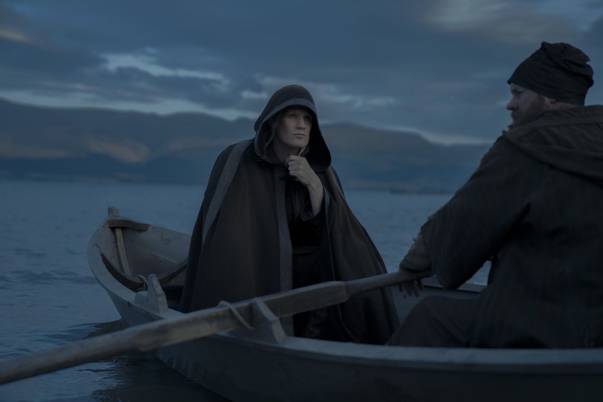 Matt Smith dans le rôle de Daemon Targaryen, portant une grande cape avec une capuche et voyageant dans un petit bateau dans House of the Dragon