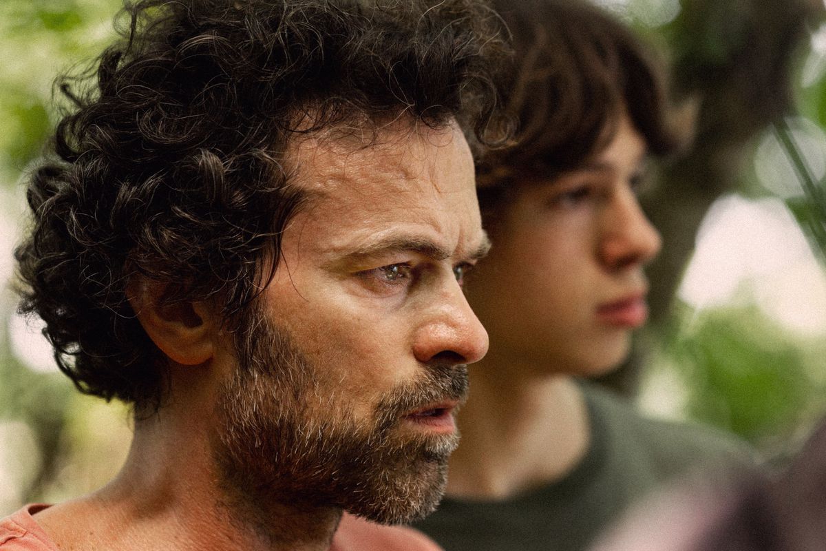 Romain Duris et Paul Kircher, debout dans une forêt, regardent avec surprise quelque chose hors champ dans The Animal Kingdom