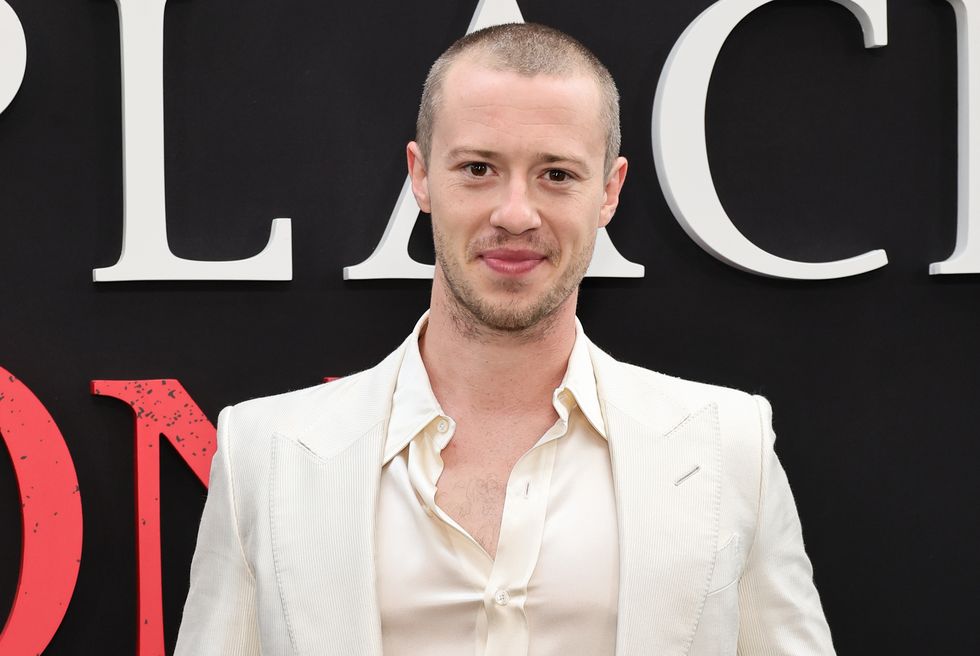 Joseph Quinn sourit à la caméra en portant une chemise à col ouvert et un costume couleur crème