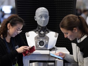 Une requête déposée cette semaine demande à la Cour fédérale du Canada de déclarer que seuls les humains – et non l’intelligence artificielle – peuvent être considérés comme des auteurs en vertu de la loi canadienne sur le droit d’auteur. Des gens consultent leur téléphone pendant qu’AMECA, un robot IA, regarde la conférence All In sur l’intelligence artificielle, le jeudi 28 septembre 2023 à Montréal. LA PRESSE CANADIENNE/Ryan Remiorz