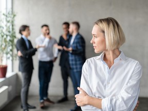 Des collègues masculins chuchotent dans le dos d'une femme d'affaires mécontente au bureau