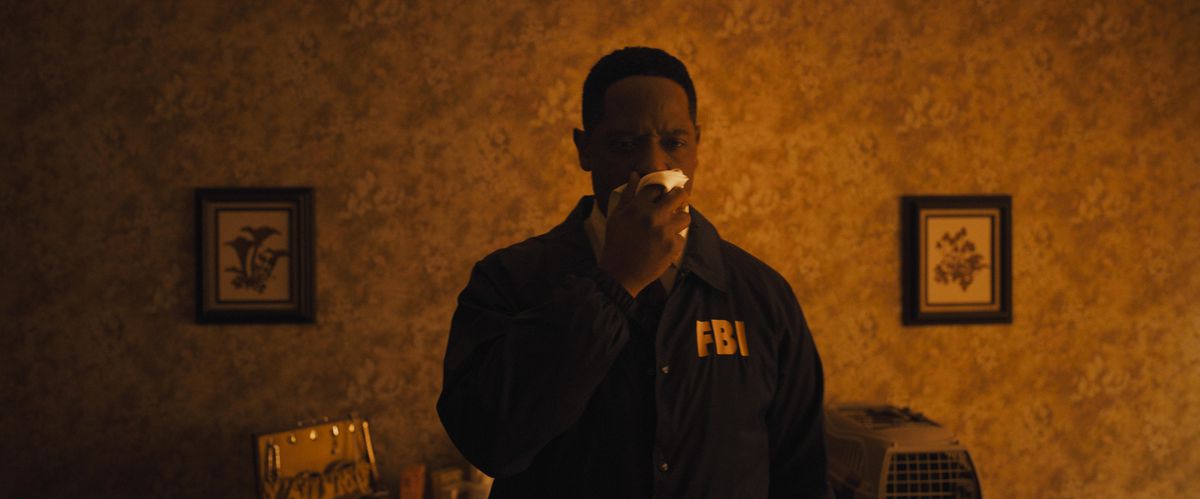 Blair Underwood dans le rôle de l'agent Carter dans Longlegs tenant un chiffon devant son nez et regardant vers une scène de crime hors écran