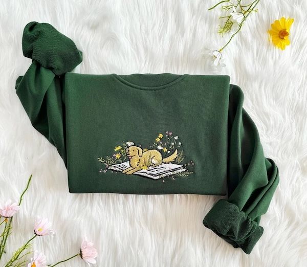 pull ras du cou vert avec un motif brodé d'un chien noir et de fleurs reposant à l'intérieur d'un livre