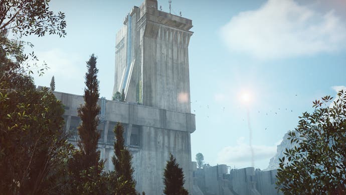 Capture d'écran d'ARC Raiders montrant une grande tour en béton sous un ciel bleu vif. Des montagnes sont visibles en arrière-plan tandis qu'un épais feuillage vert est visible au premier plan.