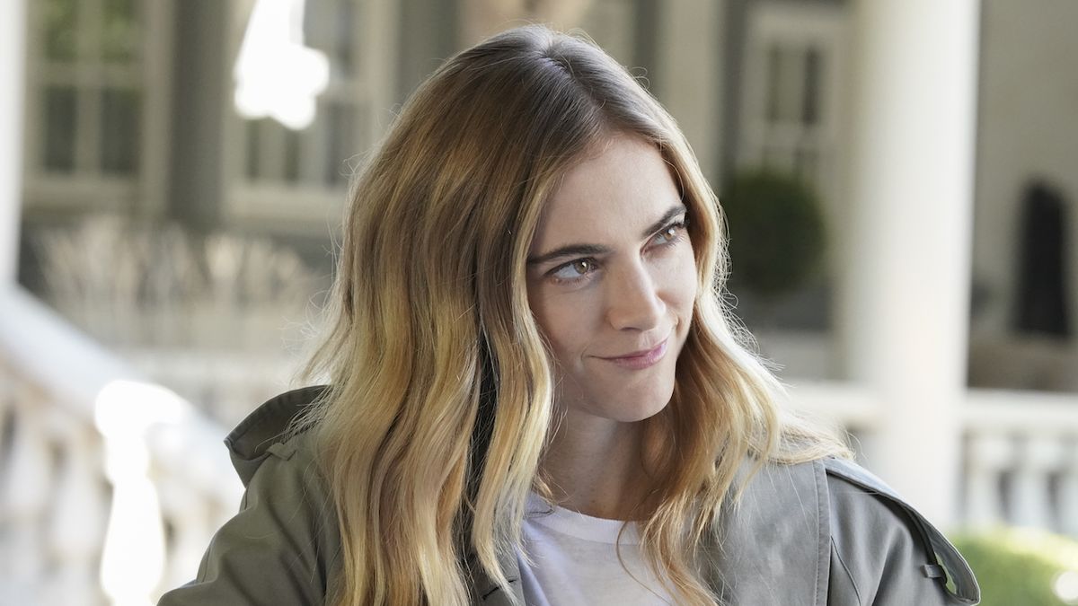 Emily Wickersham smirking and standing near large white house in NCIS