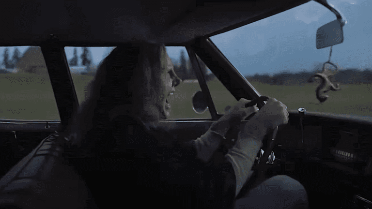 Nicolas Cage in heavy prosthetics driving a car in Longlegs 