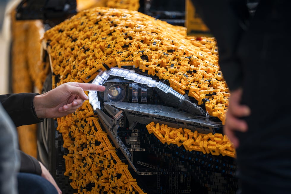 une personne pointe du doigt les phares grandeur nature de la McLaren P1 en Lego Technic avec sa main gauche