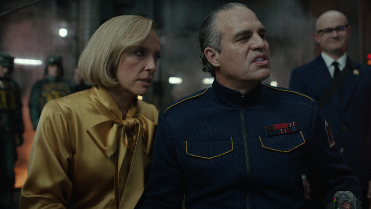 Toni Collette se penche pour parler à un Mark Ruffalo ricanant et en uniforme dans Mickey 17.