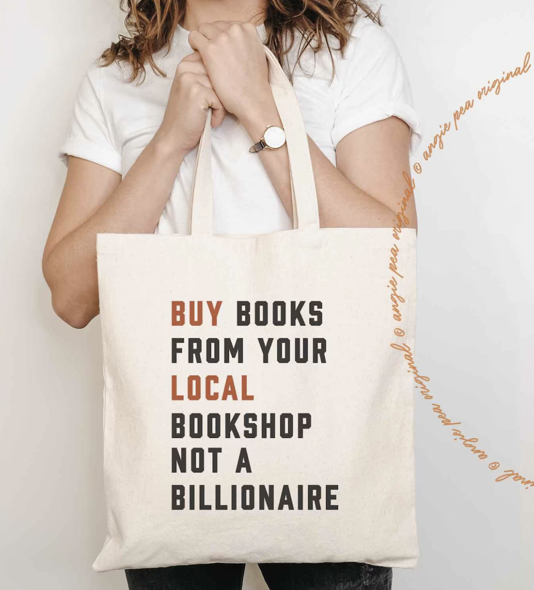 Image de quelqu'un tenant un sac fourre-tout de couleur crème avec "achetez des livres dans votre librairie locale, pas chez un milliardaire" sérigraphié sur le devant