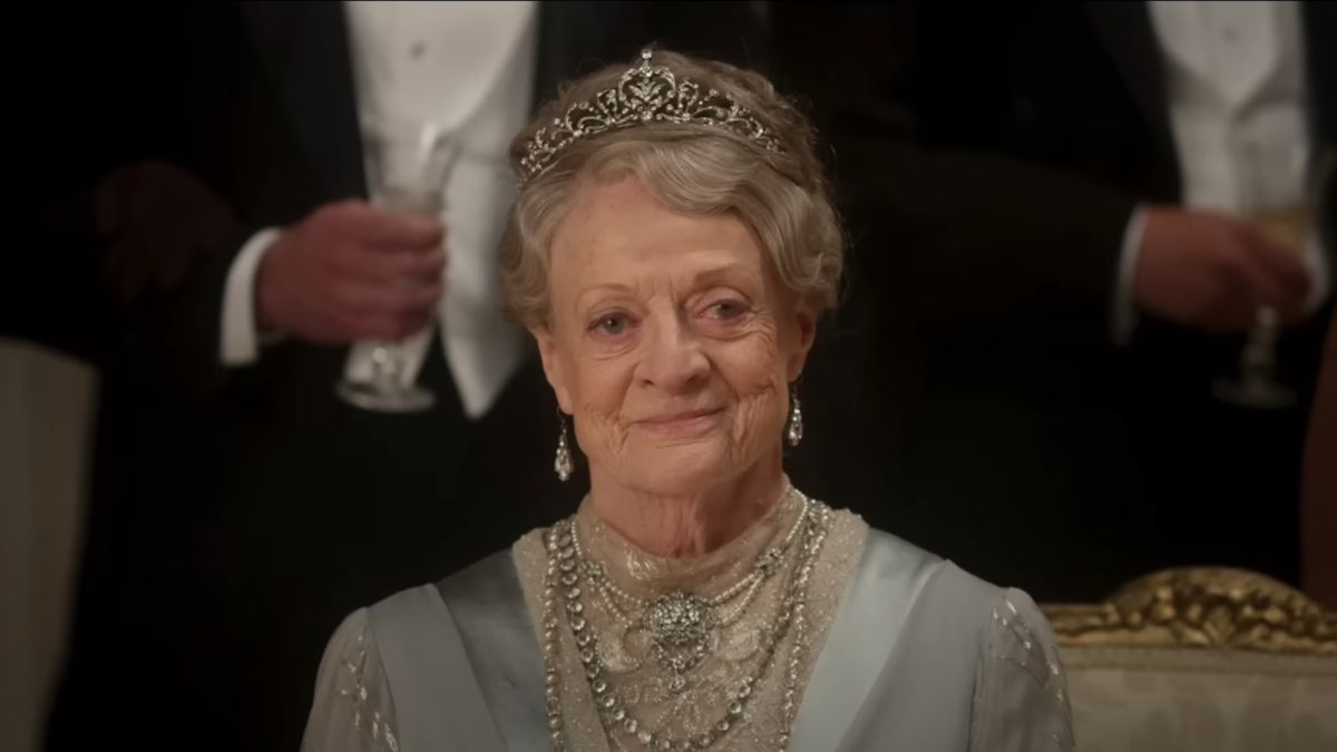 Dame Maggie Smith sits dressed in her finest smiling at a ball in Downton Abbey: The Movie.