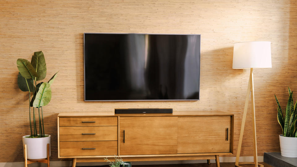 Plan large d'un téléviseur monté sur un meuble TV avec la barre de son Bose Smart Soundbar posée sur un meuble de divertissement en dessous. Fougère en pot à gauche, lampe à droite.