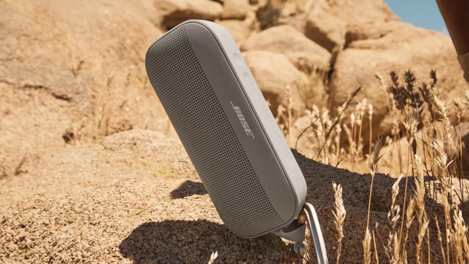 Le Bose SoundLink Flex défie la gravité car il se trouve à un angle contre les broussailles du désert sur une colline rocheuse. Image marketing du style de vie du produit.