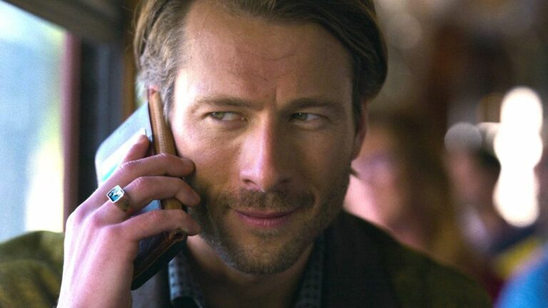 Glen Powell's Gary Johnson speaks on a phone in a close-up photo of his face in a press image for the Netflix movie Hit Man.