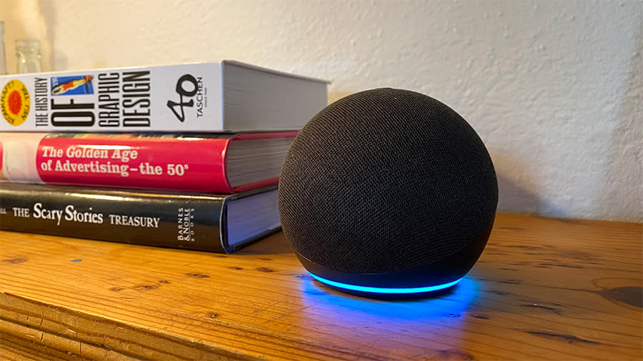 L’enceinte intelligente Echo Dot se trouve sur une étagère en bois à côté d’une pile de livres. 