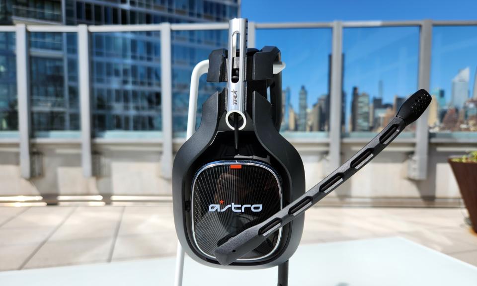 Le casque de jeu Astro A40 TR repose sur un support blanc sur une table extérieure, avec son microphone intégré étendu.